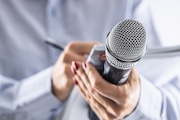 A journalist holds a microphone at a press conference and writes information in a notebook